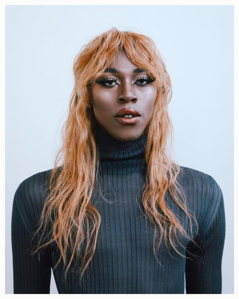 a black women with orange hair and long fake lashes is staring directly into the camera 
