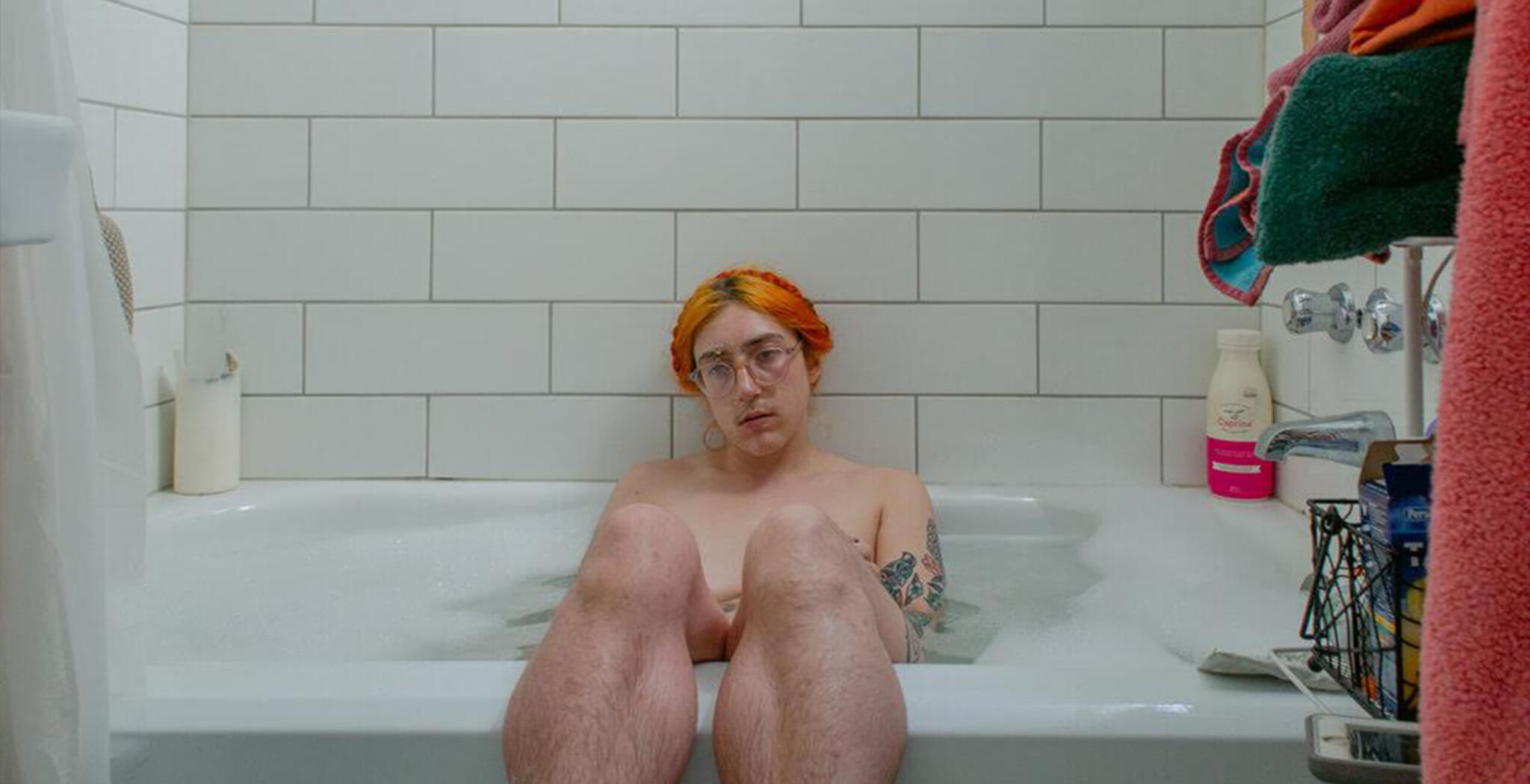 A person, Laurence Philomène, is sitting in a bathtub. They have bright red hair