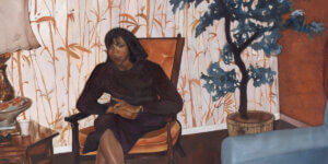 Painting of a woman sitting in an armchair against patterned wallpaper with a potted tree nearby; intimate domestic scene suggesting migration, memory, and stillness.