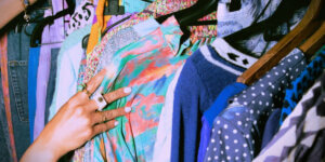 A person browses a colorful rack of vintage and secondhand clothes, showcasing eclectic patterns and textures, symbolizing sustainable fashion choices.