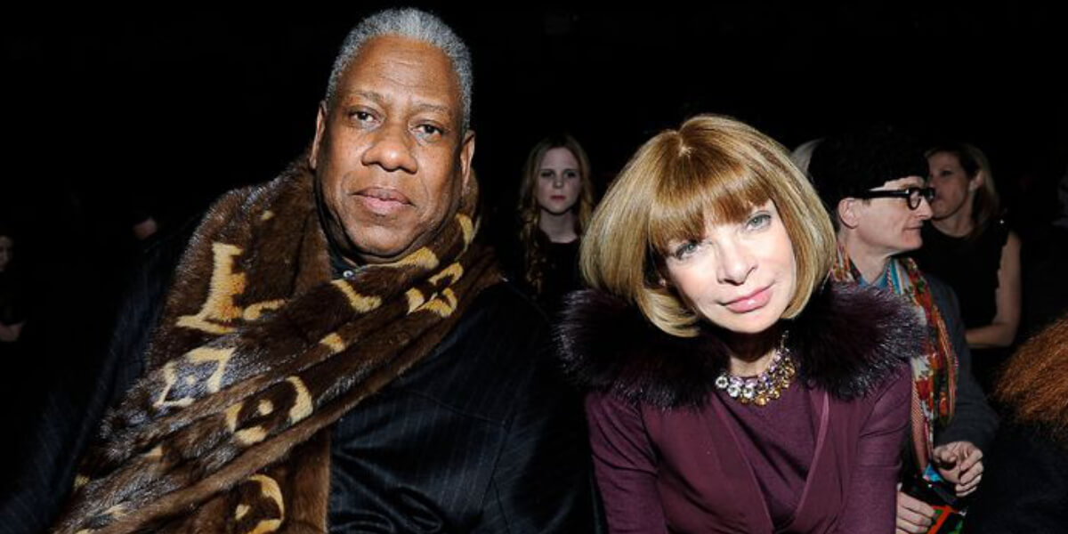 Two prominent fashion editors, André Leon Talley and Anna Wintour, seated front row at a fashion show, dressed in elegant, luxurious winter attire.