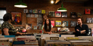 Three characters from the show "High Fidelity" including Zoe Kravitz, talking in an indie record store surrounded by vinyl records, symbolizing the analog media resurgence.