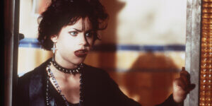 Character in dramatic Goth style with dark makeup, black choker, and layered jewelry, reflecting 1990s Goth subculture fashion.