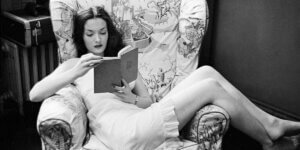 Woman in vintage setting reading a book while lounging in an armchair – symbolizing reflective summer reading.
