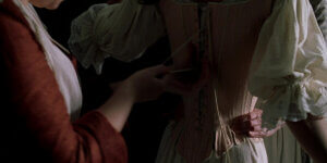 Hands tightening strings on a white cotton corset, symbolizing historical fashion and cultural heritage.