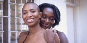 Two people share a warm, intimate embrace, symbolizing connection, care, and queer community in contemporary creative spaces.