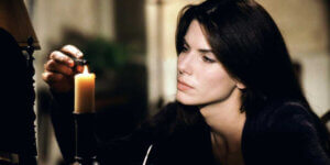 Sandra Bullock lighting a candle in a dimly lit room, reflecting on loss and memory — a still from Practical Magic (1998), a film evoking autumn’s themes of love, grief, and the supernatural.