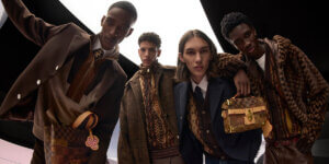 Four models wearing layered fall menswear in rich brown tones featuring tailored jackets, textured knits, and monogram accessories from Louis Vuitton’s Fall/Winter collection, representing timeless luxury and mindful fashion choices.