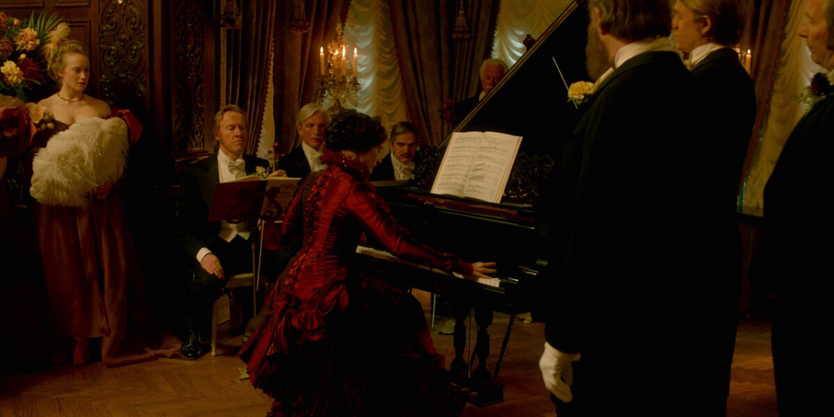 Gothic ballroom scene from Crimson Peak featuring Lucille Sharpe performing at the piano in her iconic red gown, showcasing the film’s Victorian costume design.
