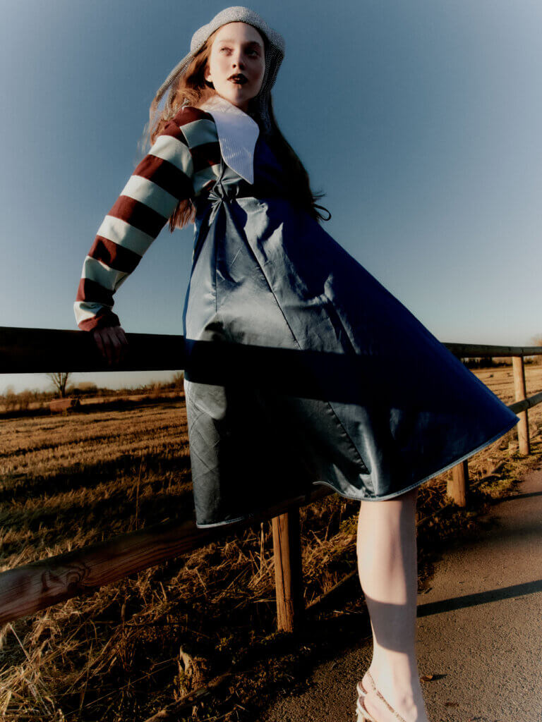 Fashion editorial set in the Italian countryside featuring a model in a soft knit look and statement accessories, styled against winter fields with a floral headpiece, photographed by Pietro Groff.
