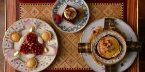 Top-down view of ornate plated desserts with gold leaf, fruit, and fine china, representing luxury food aesthetics and culinary art history.