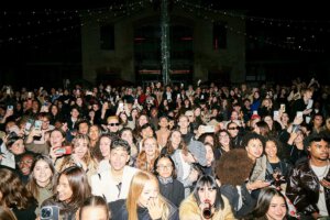 Large crowd of Gen Z attendees filming a nighttime fashion event with smartphones at an outdoor runway show