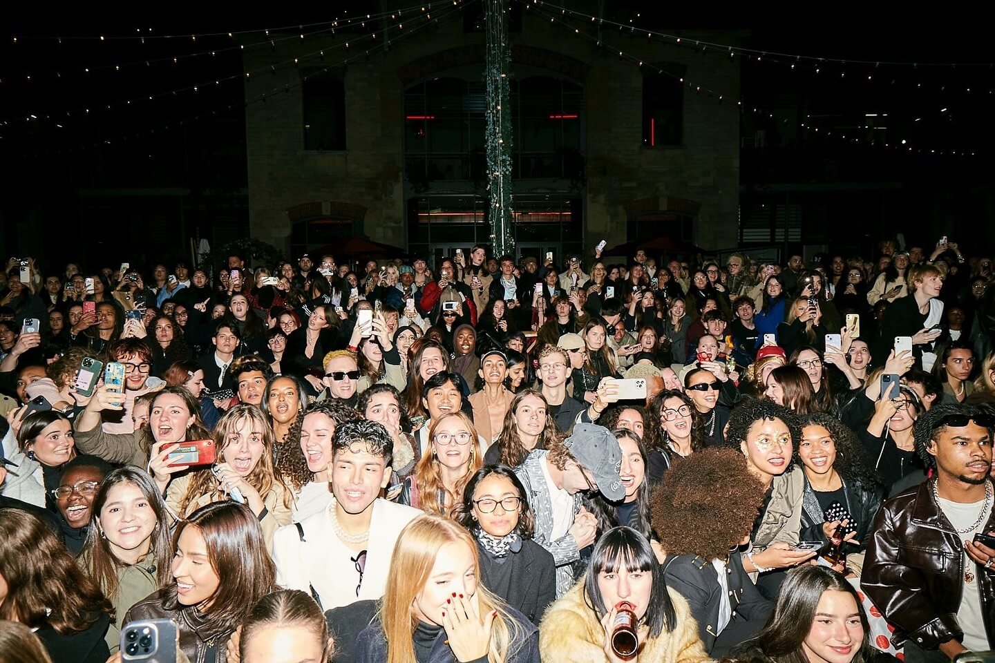 Large crowd of Gen Z attendees filming a nighttime fashion event with smartphones at an outdoor runway show
