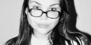 Portrait of Sere Rivérs in her studio surrounded by blue-toned paintings, ceramics, and poetic artworks exploring vulnerability and self-expression