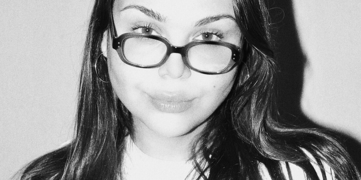 Portrait of Sere Rivérs in her studio surrounded by blue-toned paintings, ceramics, and poetic artworks exploring vulnerability and self-expression