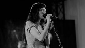 Black and white photo of Holly Humberstone singing live into a microphone during an intimate performance