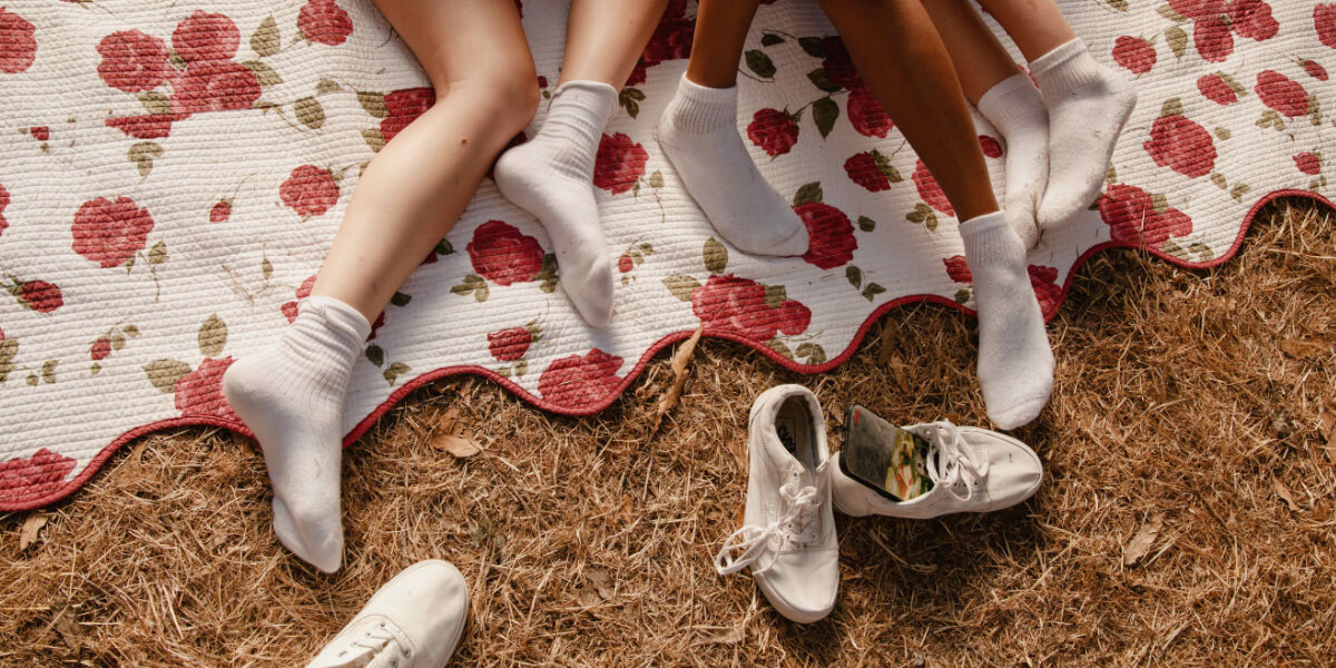 Close-up of friends' legs and feet on a vintage floral rose picnic blanket, symbolizing the human connection and intimacy discussed by Erika Lust.