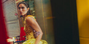 Model in a gold velvet dress walking through Les Puces de Saint-Ouen in Paris, framed by reflections and vibrant colors, photographed by Charles Hemon for TITLE Magazine's "A New Way of Seeing" editorial.