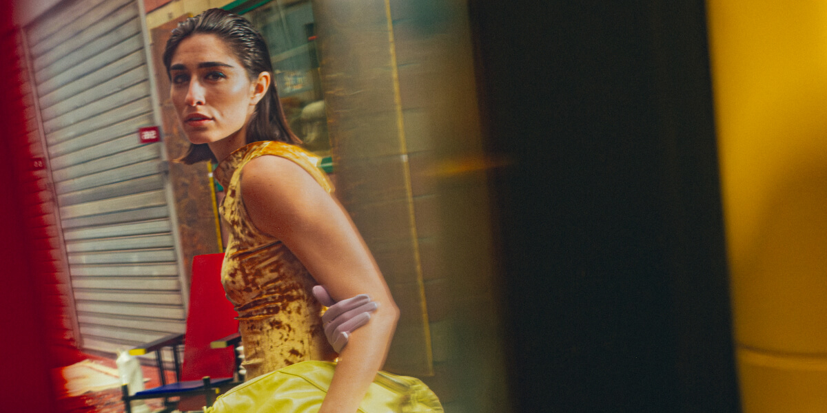 Model in a gold velvet dress walking through Les Puces de Saint-Ouen in Paris, framed by reflections and vibrant colors, photographed by Charles Hemon for TITLE Magazine's "A New Way of Seeing" editorial.