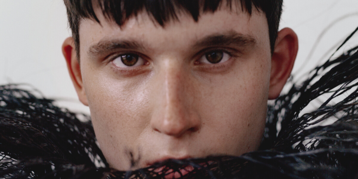 Portrait of photographer Agustín Farías wearing a black feathered garment for TITLE Magazine interview about An Hour Until They Woke You and the ЯESET issue