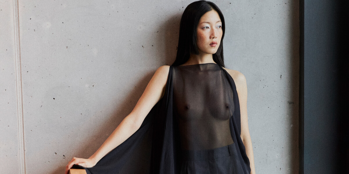 Model wearing a sheer black MALAIKARAISS dress from the Playground Love Spring Summer collection during Berlin Fashion Week, showcasing minimalist sustainable fashion by designer Malaika Raiss.