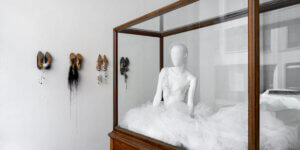 Bridal-inspired couture mannequin by Lou de Bètoly displayed in a glass case alongside repurposed vintage heels transformed into sculptural wall jewelry during the designer's Berlin Fashion Week showroom exhibition.