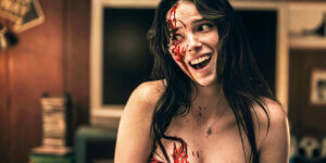 Bloodied woman smiling in a horror film scene, representing female rage, femininity and the female monster in feminist horror cinema.