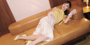 Ariana Grande reclining on a leather sofa in a yellow top, sheer floral skirt and gloves