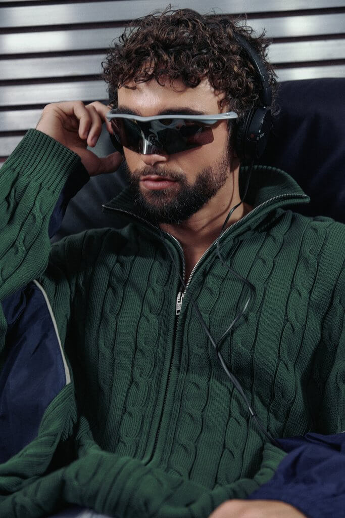 Arda Saatçi wears a green sweater, sunglasses and headphones in TITLE Magazine’s Berlin Psycho fashion editorial