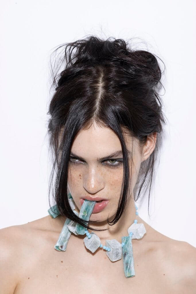 Beauty editorial portrait of a model wearing an avant-garde turquoise and white necklace with dramatic eye makeup and an undone updo.