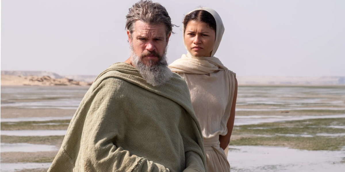 Matt Damon and a woman in historical Greek-inspired costumes standing in a desert landscape, inspiring Halloween costume ideas from The Odyssey